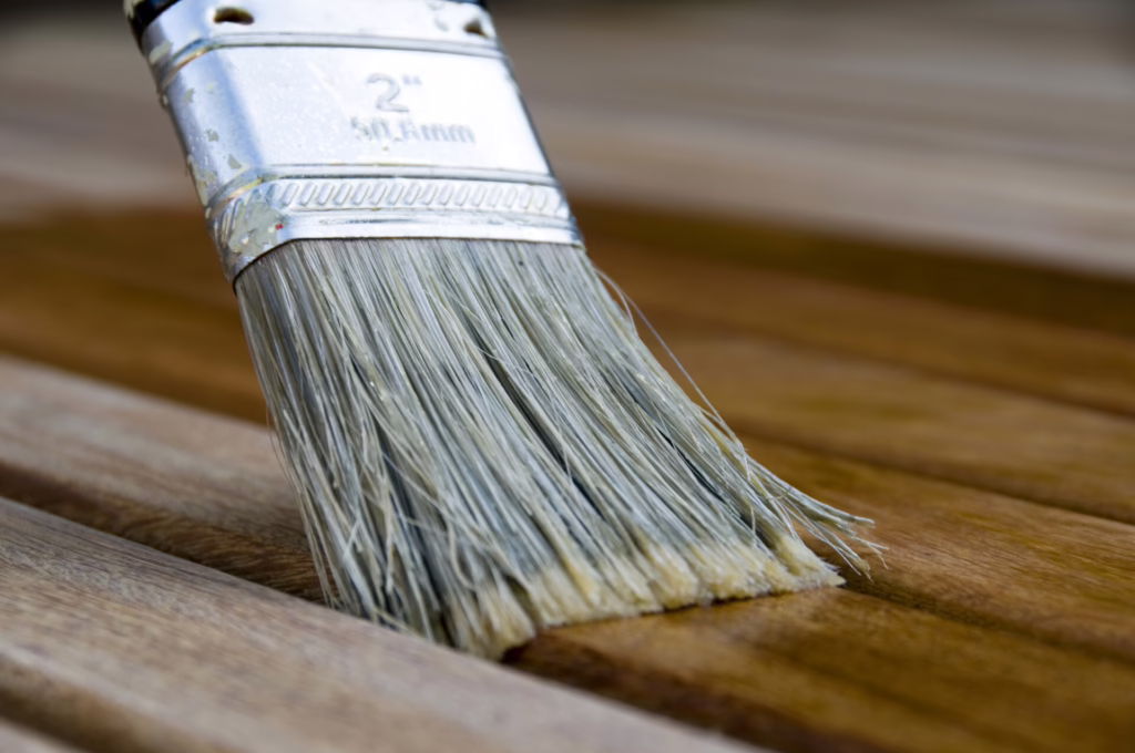 Das Bild zeigt eine Nahaufnahme von einem Lackierpinsel, mit dem Holz in einem transparenten Lack bearbeitet wird.